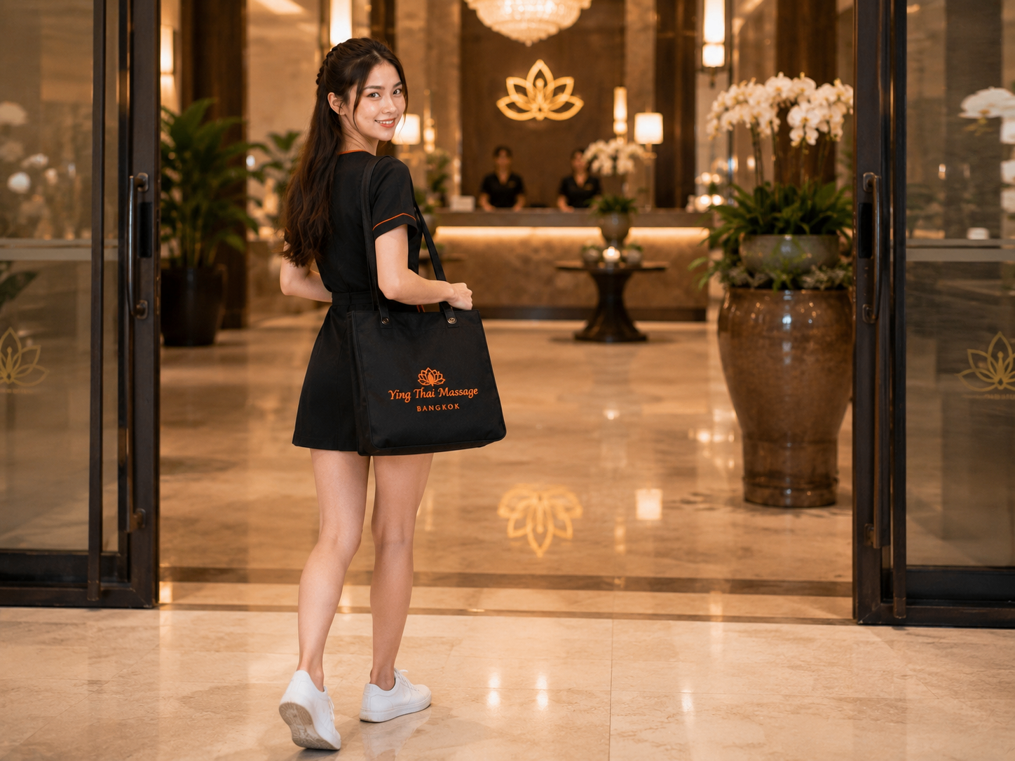 Ying Thai therapist arriving at a luxury Bangkok hotel lobby with branded tote
